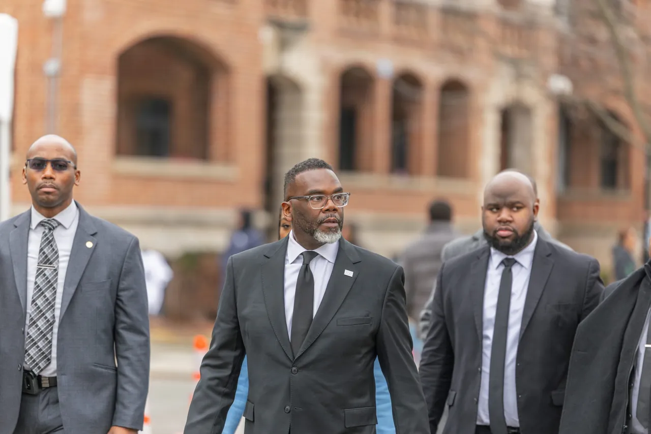 Three men in suits walk past a brick building