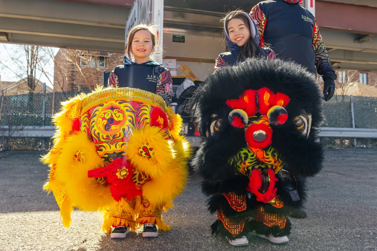 Two children stand behind yellow and black lion costumes
