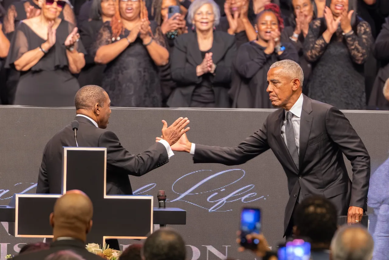 Barack Obama reaches across the stage to clasp hands with a speaker while the choir applauds behind them