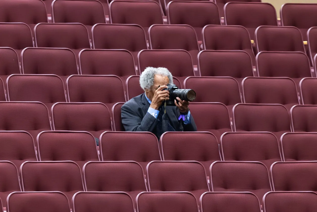 A photographer works alone among rows of empty red seats