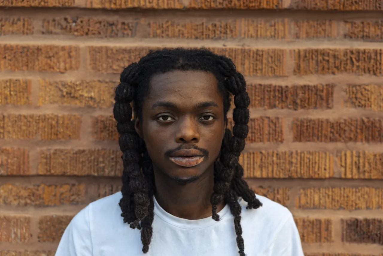 A young man with braids against a brick wall