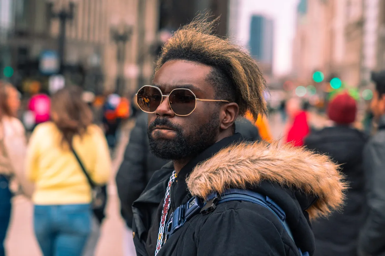 A man in sunglasses and a fur-trimmed parka on a crowded downtown street