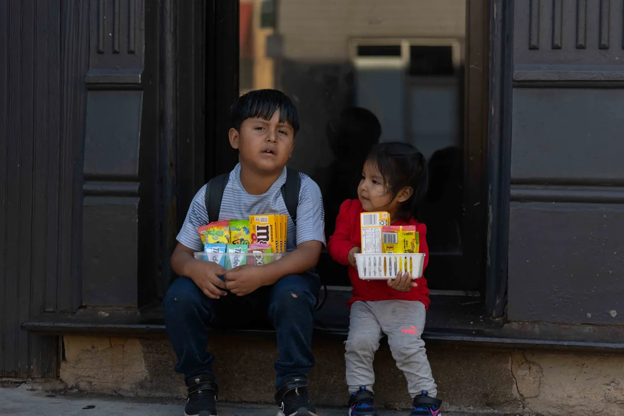 Two children sit on a doorstep holding snacks
