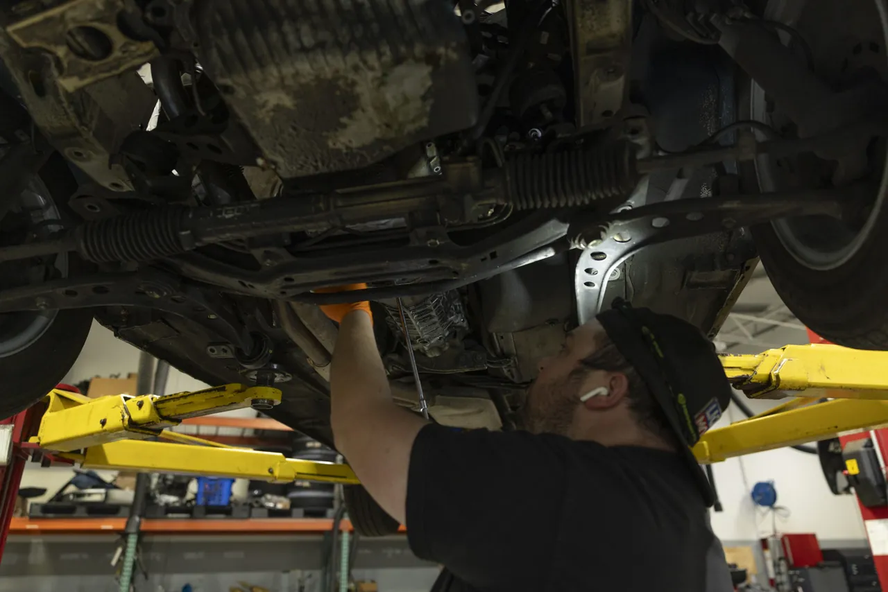 A mechanic reaches into the underside of a car on a lift