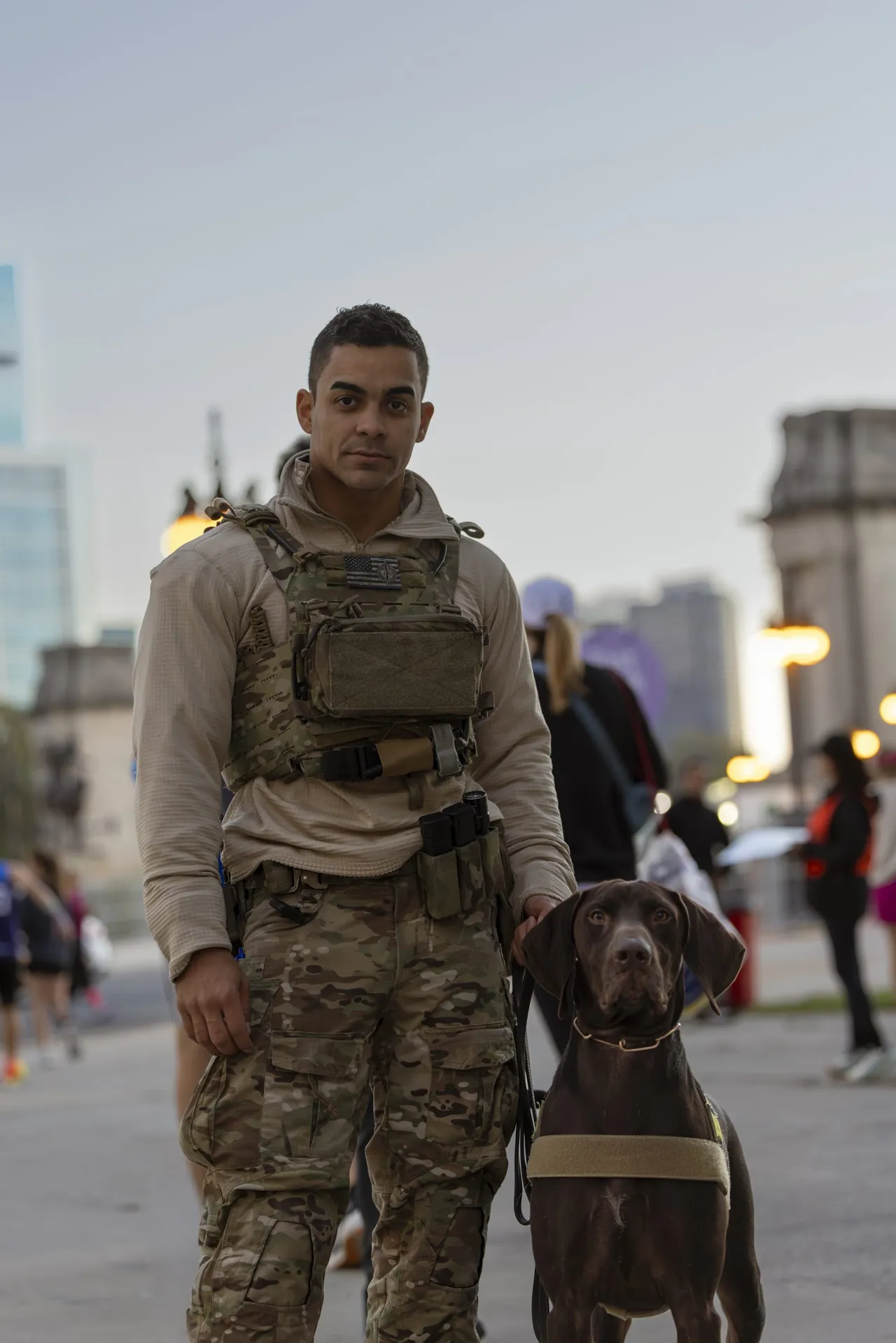 An officer in tactical gear stands with a police dog before dawn