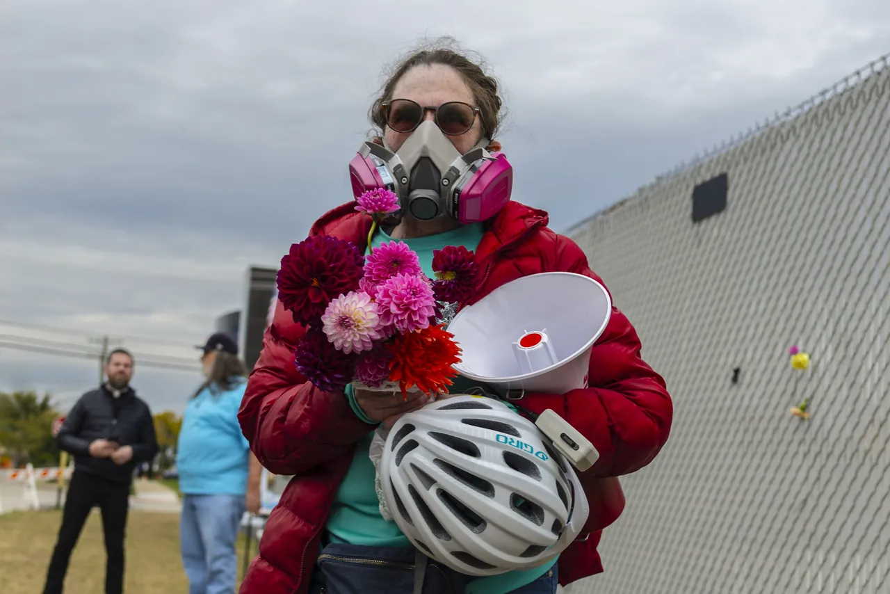 A demonstrator in a respirator holds flowers, a megaphone and a bike helmet