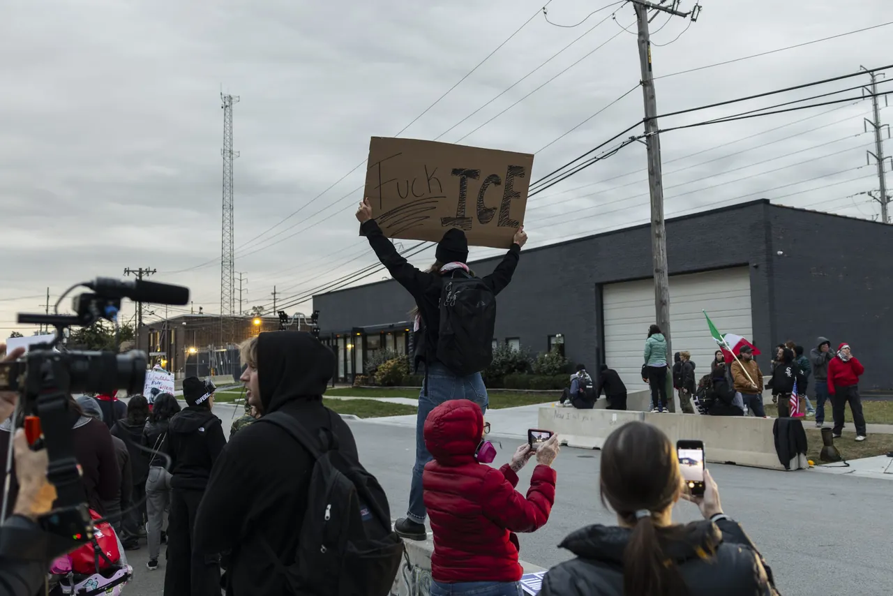 A demonstrator holds a sign overhead while news cameras film
