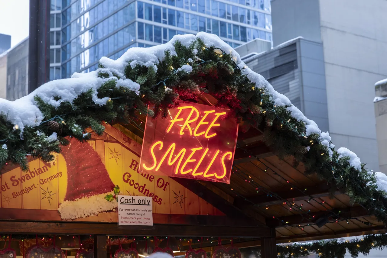 A neon sign reading Free Smells on a snow-covered market hut