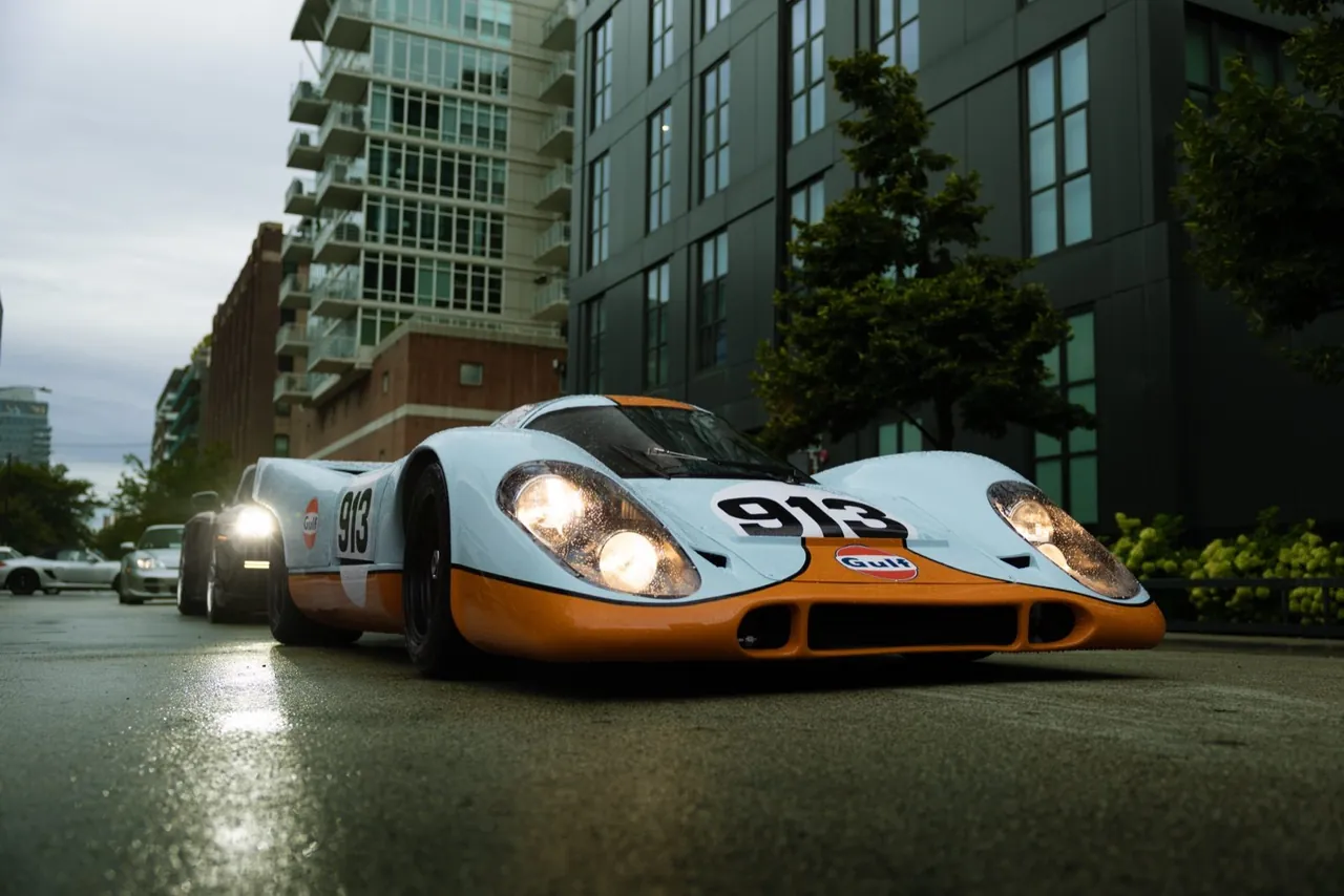 A Gulf-liveried Porsche 917 with its lights on, on a city street