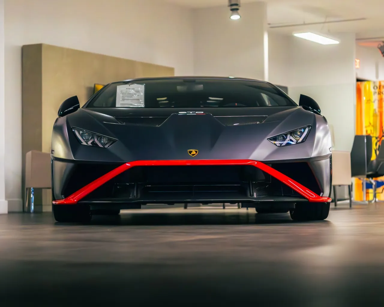 A dark Lamborghini with a red splitter in a showroom